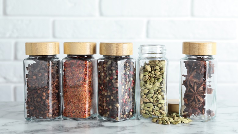Whole spices in mini mason jars on marble counter.