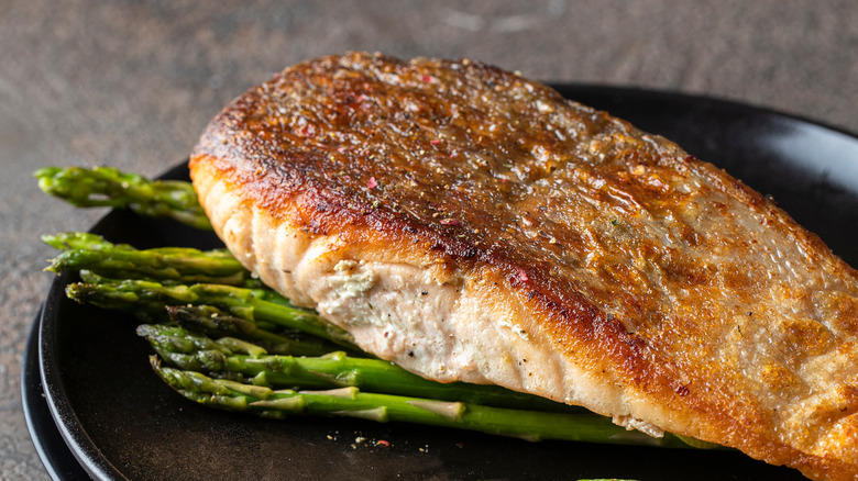 Cooked salmon with crisp skin on black plate with asparagus