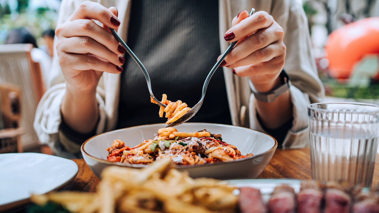 Hands with nail polish on the fingers use a fork and spoon to twirl spaghetti at a restaurant table
