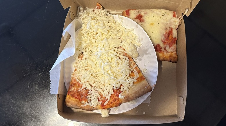 Slice of pizza topped with cold cheese in a pizza box