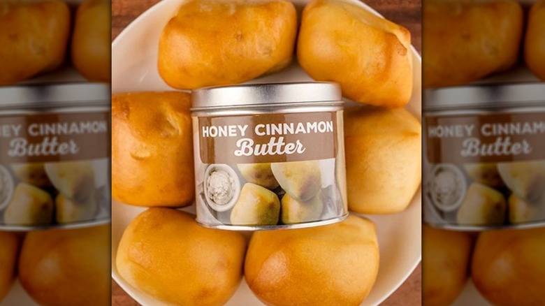 Honey Cinnamon Butter candle in metal container surrounded by Texas Roadhouse rolls