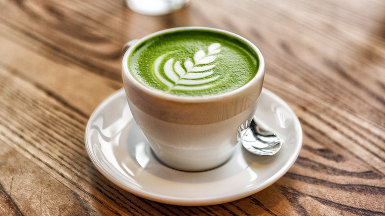 A matcha latte with latte art on a wood table