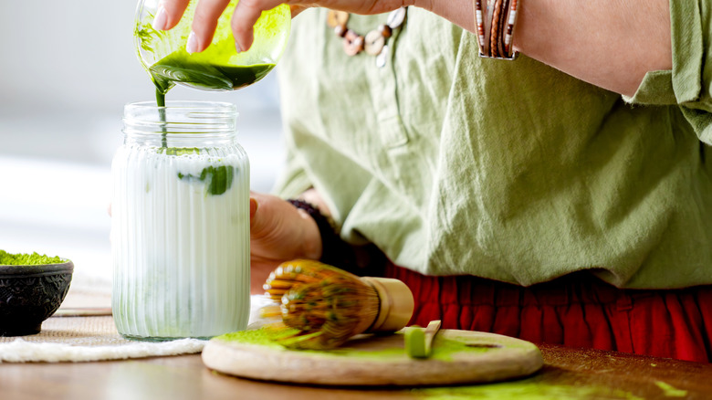 A person pouring matcha into a glass of milk