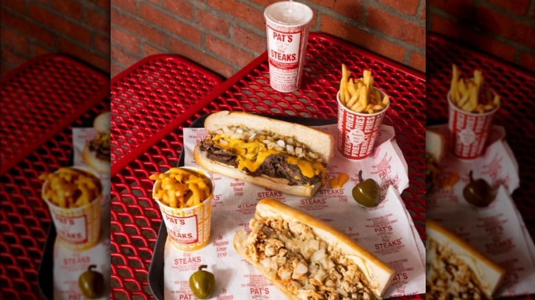 Pat's King of Steaks cheesesteak sandwich sits next to plain and cheesy fries as well as a big pepper