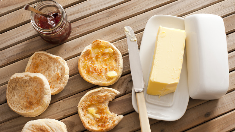 Butter in butter dish on table top by English muffins and jam