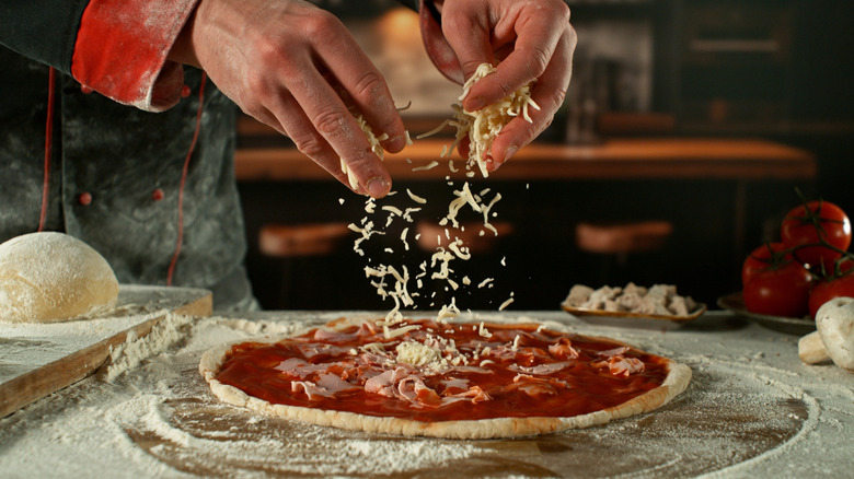 Hands dropping shredded mozzarella on a pizza being made