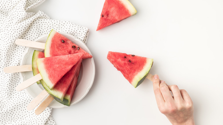 Person holding watermelon slice on a stick