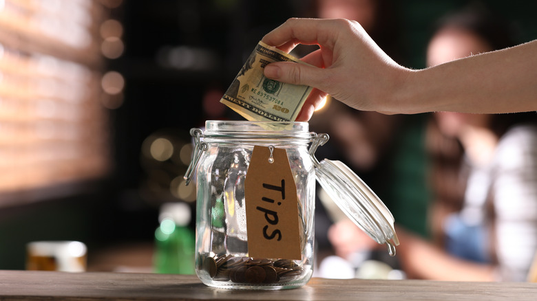 Hand putting twenty dollar bill in glass tip jar