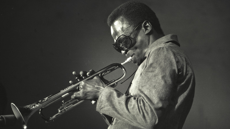 Black and white profile photo of Miles Davis playing a trumpet.