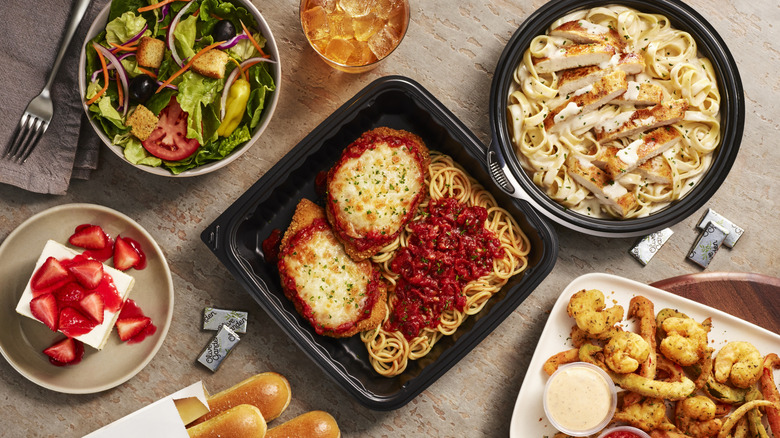 A table full of Italian food, including a salad, pasta, an iced tea, garlic bread, seafood, breadsticks, and a strawberry cake