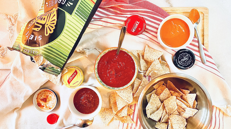Three bowls of salsa with tortilla chips on a tablecloth