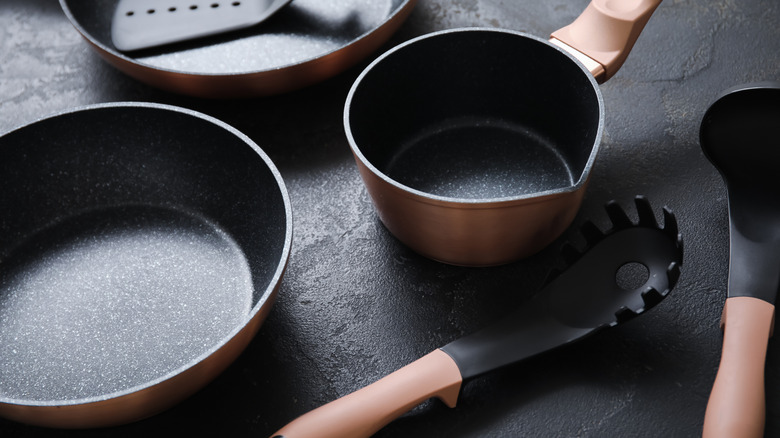A variety of pots, pans, and kitchen utensils sit on black slate