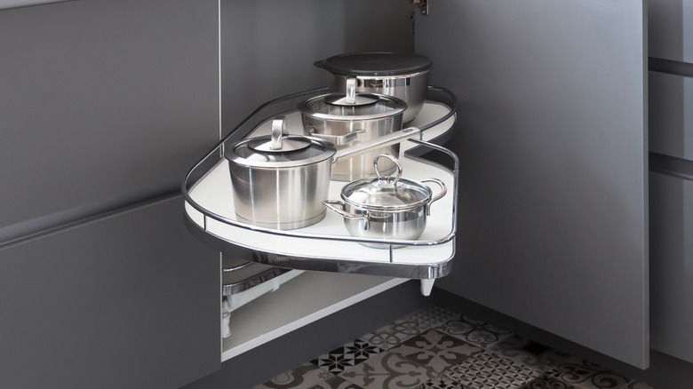 A kitchen cupboard door opens to reveal a pull-out organizer with pots on it