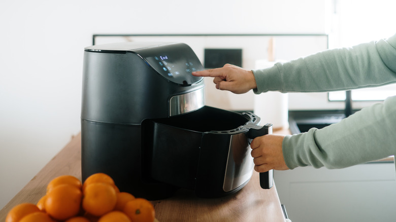A man pulls out the basket of an air fryer with one hand while pressing a button with the other