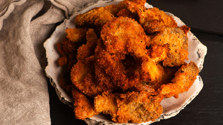 Crispy fried oysters sit on a shell-like plate with burlap next to it