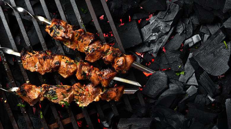 Grilled pork kebabs on metal skewers over charcoal.