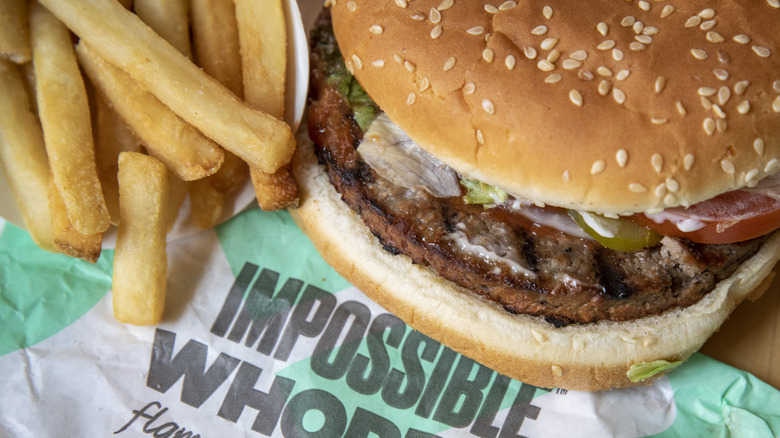 A plant-based Impossible Whopper sits on a wrapper next to french fries.
