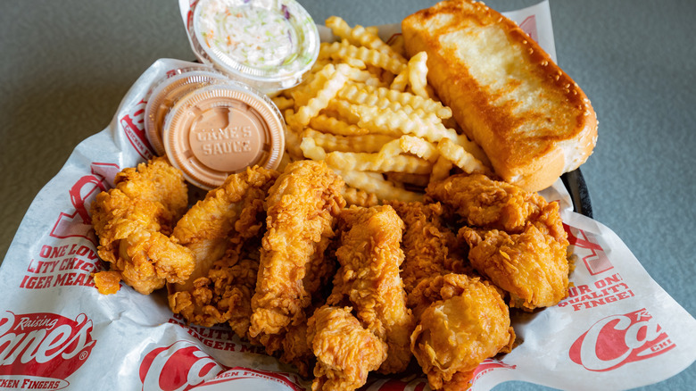 Raising Cane's chicken fingers, fries, Texas Toast, coleslaw, and Cane's sauce in a basket with the chain's branded paper