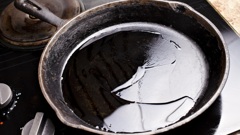 An old cast-iron pan with oil inside sits on a stovetop