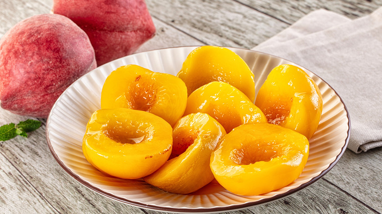 canned peaches in a heavy syrup rest in a bowl next to fresh peaches and mint
