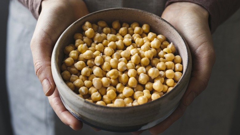 Two hands cupping a ceramic bowl filled with cooked chickpeas