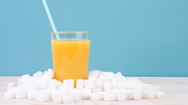 A glass of orange juice surrounded by cubes of sugar