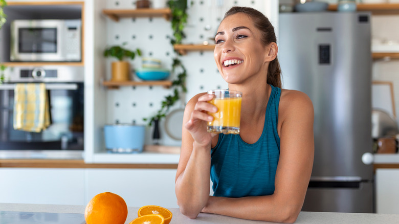 A person enjoys a glass of orange juice in the kitchen