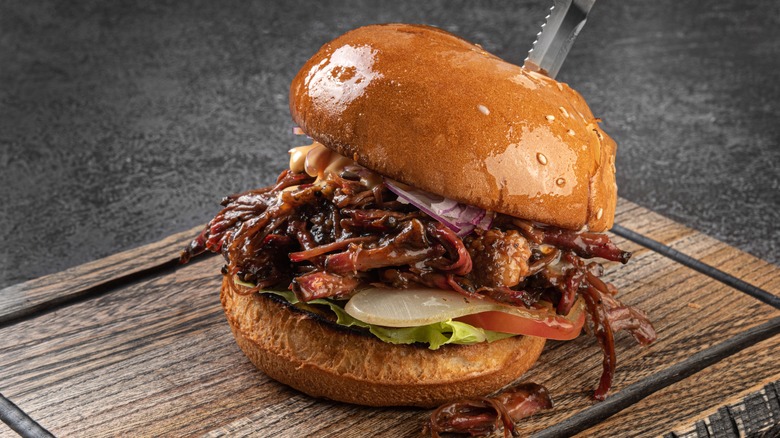 A pulled pork sandwich with onions, lettuce, and sauce