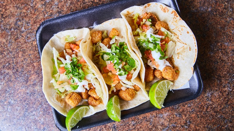 Three fried tilapia fish tacos with lime on a black tray