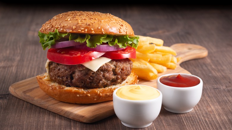 Burger on wooden serving board with condiments and fries