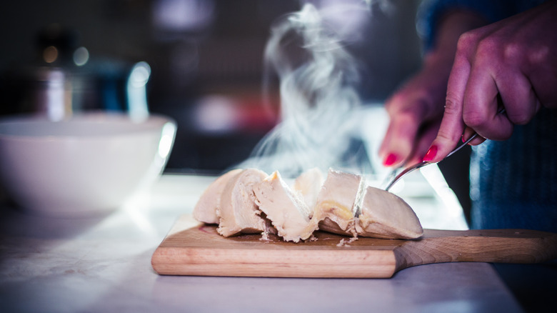 A diner uses a knife and fork to cut into cooked chicken on a cutting board