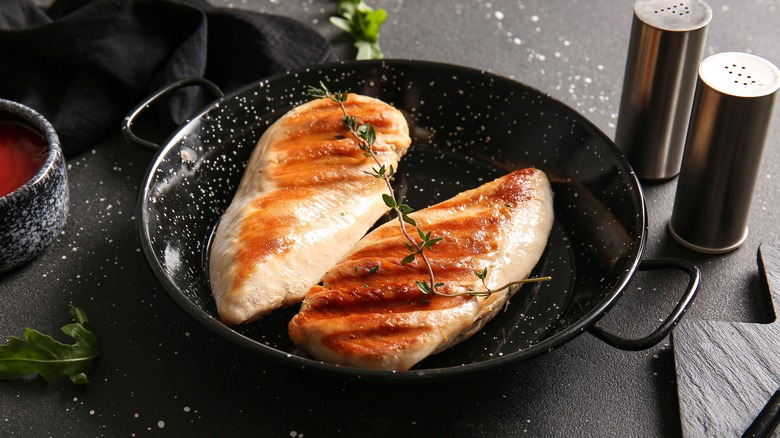 Two browned chicken breasts rest in a pan with a sprig of thyme on them