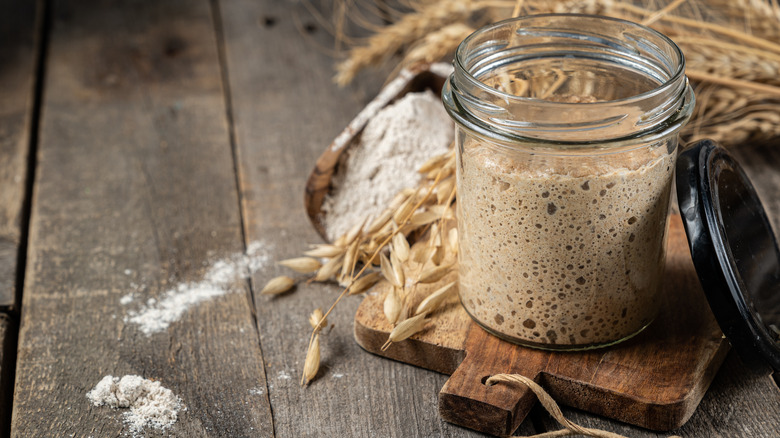 sourdough starter in a jar on wooden plant surrounded by wheat and flour