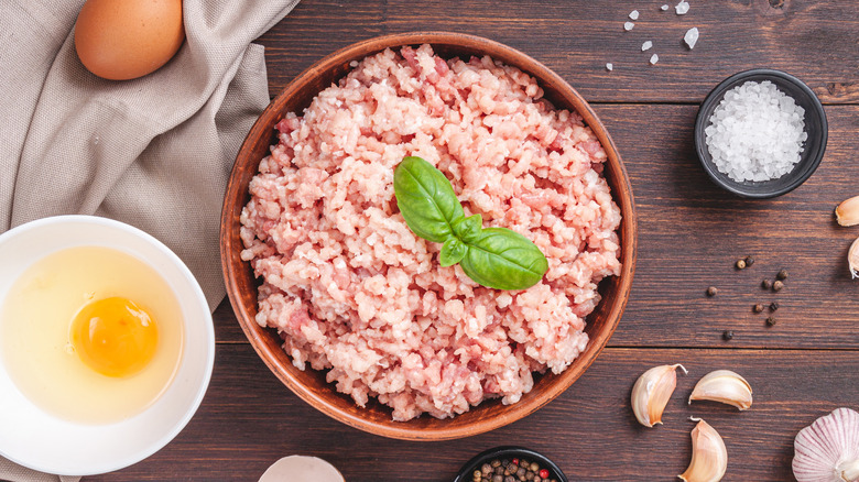 Raw ground turkey meat in a bowl with a raw egg, garlic, and seasoning