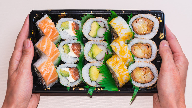 Two hands holding package of sushi