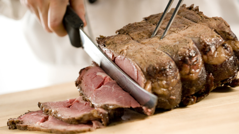 Prime rib being carved on a wooden cutting board