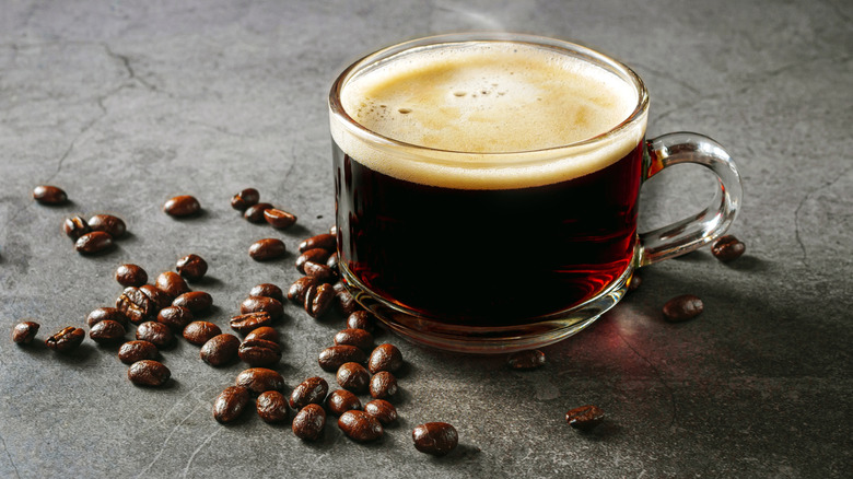 Coffee in a clear glass cup with scattered coffee beans around it