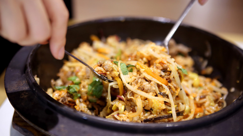 Person mixing bibimbap ingredients in a bowl.