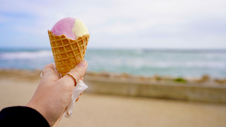 Someone holds an ice cream cone up at the beach