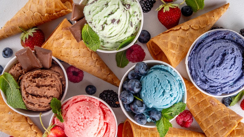 Various flavors of ice cream in cups are surrounded by berries and empty ice cream cones