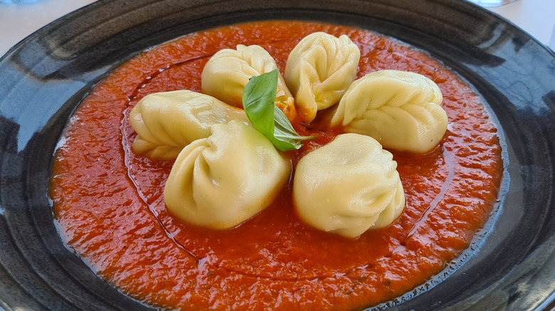 A plate of culugiones in a tomato sauce with fresh basil and a drizzle of olive oil.