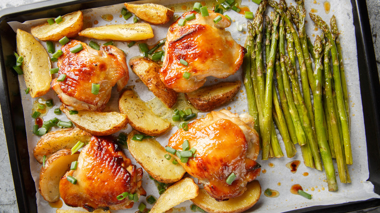 Glazed chicken thighs sit next to potato wedges and asparagus.