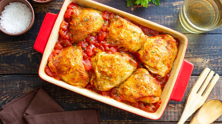 Chicken thighs sit in a casserole dish with tomatoes