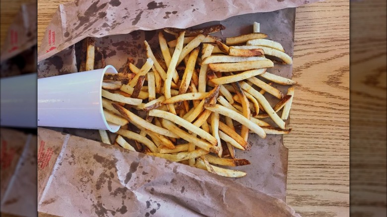 A cup of Five Guys fries spilled into a ripped paper bag.