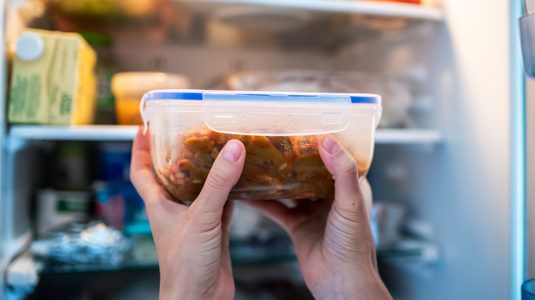 A person holds a locked-lid container with both hands in front of an open fridge