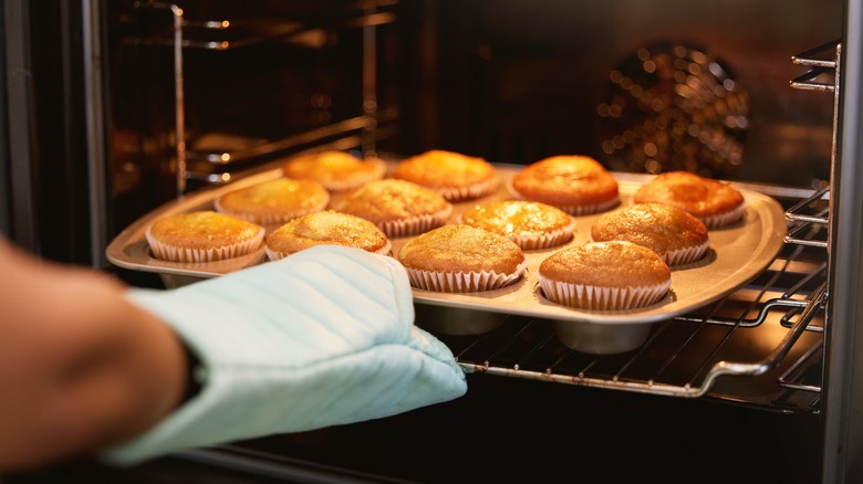 A hand reaches to take muffins out of an oven