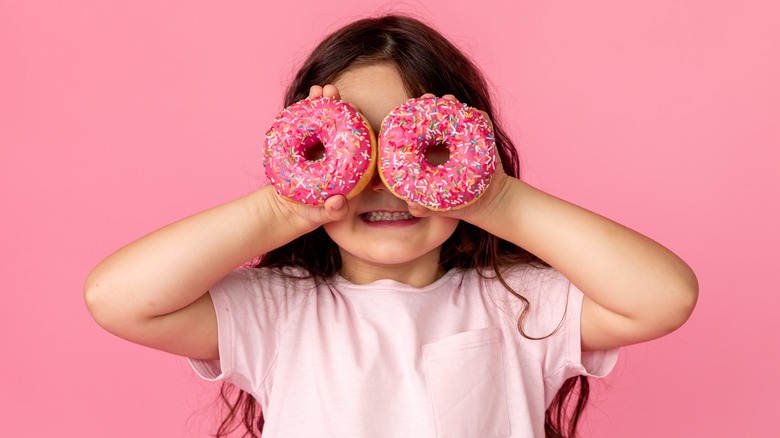 little girl holds two donuts
