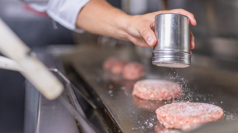 Chef salting burger patties on a hot griddle