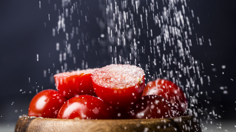 Cherry tomatoes in a bowl receive a healthy sprinkling of salt