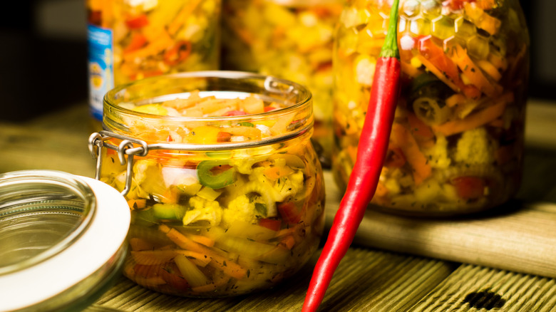 Jar of giardiniera next to a long red pepper.